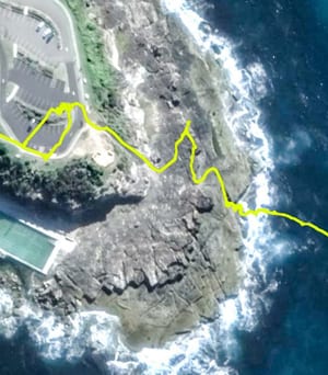 Aerial view of the rocky Freshwater headland in Sydney, with lines of white surf breaking along its ocean edge and an ocean pool cut into the shoreline.